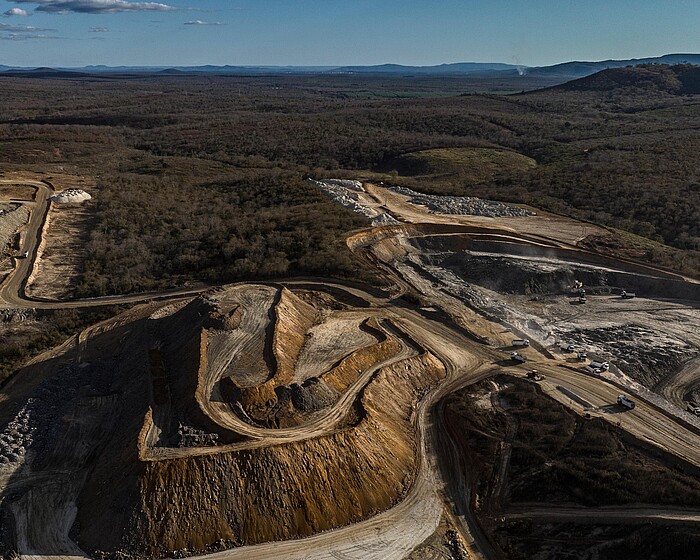 The Sigma Lithium Xuxa mine near Itinga, Minas Gerais state, Brazil. Steep slopes, tracks and deposits are visible in the foreground, with dense forest and blue sky in the background.